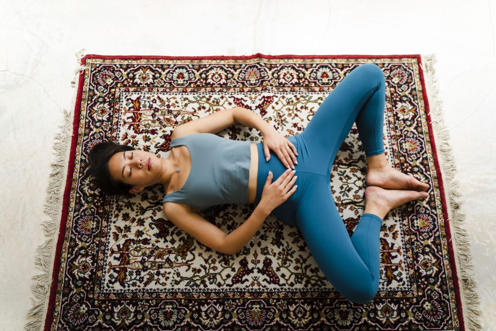 A woman practising yoga, meditating and stretching lying on a carpet indoors.